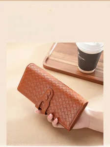 Dettaglio di un portafoglio in pelle intrecciata marrone tenuto in mano vicino a una tazza