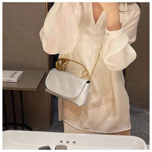 Detail of silver flap bag featuring a unique oversized gold safety pin metal handle
