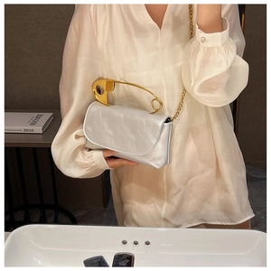 Detail of silver flap bag with large gold safety pin handle and metal chain strap