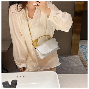 Detail view of a silver mirror square bag with a creative gold safety pin handle and chain