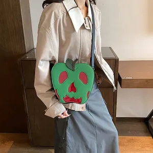 Detail of green apple-shaped crossbody bag featuring a red skull face and zipper closure