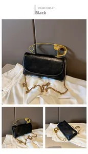 Macro view of black leather handbag featuring unique gold oversized safety pin handle