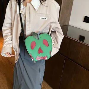 Detail of green apple-shaped bag featuring red skull embroidery and metal zipper