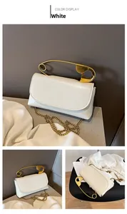 Detail of white PU leather bag with gold safety pin handle and chain strap on silk