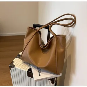 Detail of a large brown pebbled leather tote bag placed on a white suitcase for travel