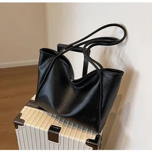 Detail of black large-capacity tote bag with pleated texture placed on a white suitcase