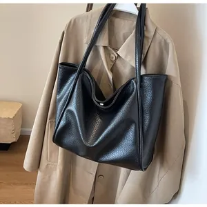 Close-up of black lychee-textured leather tote bag hanging on a stylish beige trench coat