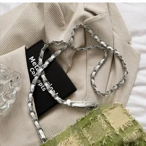 Detail of silver chain strap with white leather weave on a beige textured blazer
