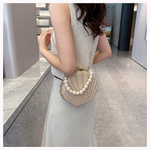 Detail view of a shell-shaped evening bag with pearl handle and golden chain strap