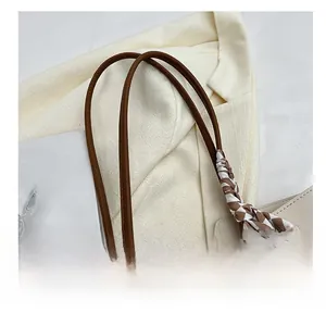 Detail of a brown leather tote handle wrapped with a checkered silk scarf accessory