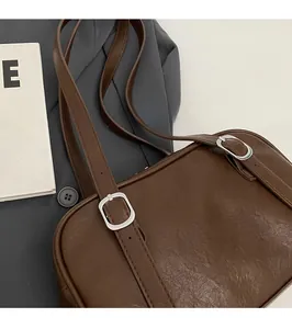 Détail des bretelles réglables et boucles argentées d'un sac à bandoulière vintage brun
