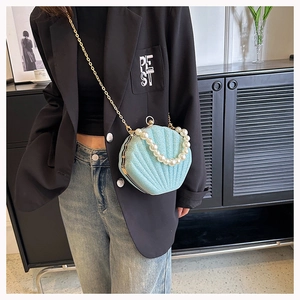 Detail of shell-shaped handbag with pearls and gold chain on model in black blazer