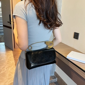 Minimalist black leather crossbody bag featuring a unique oversized gold safety pin handle