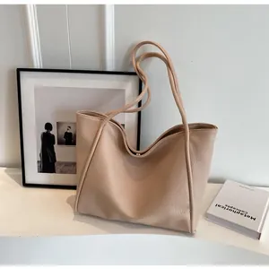 Detail of beige lychee grain leather tote bag showing slim shoulder straps and magnetic buckle