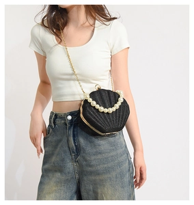Detail of a black sequined shell bag with pearl handle and golden chain on model