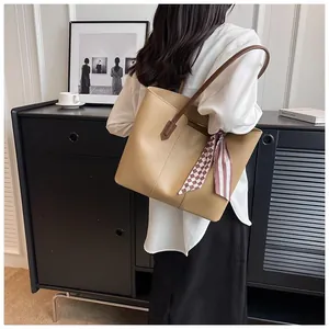 Detail of khaki leather tote bag with stylish red plaid scarf accent on the handle