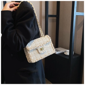 Détail du sac bandoulière en tweed avec chaîne dorée et fermoir rotatif sur blazer noir