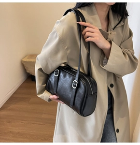 Détail d'un sac d'épaule vintage en cuir noir avec boucles argentées sur un trench beige