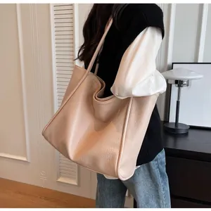 Detailed side view of large beige lychee grain leather tote bag worn by a model
