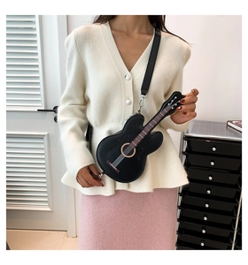 Detail of guitar-shaped black leather crossbody bag worn by a model in casual outfit
