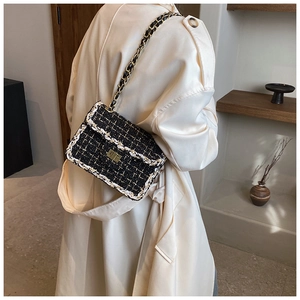 Gros plan d'un sac bandoulière en tweed noir et blanc avec fermoir doré sur un trench beige