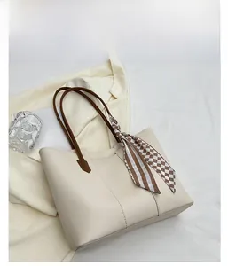 Close-up of a white PU leather tote bag featuring brown handles and a checkered silk scarf