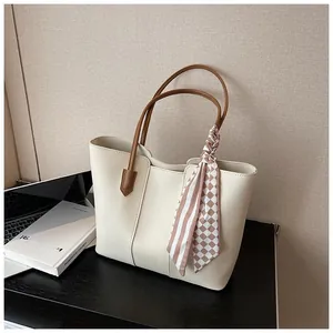 Detail of cream tote bag with brown leather handles and a plaid silk scarf accent