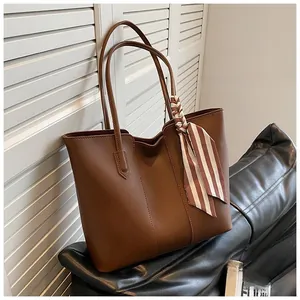 Close-up of a brown tote bag featuring a decorative striped twilly scarf on the handle