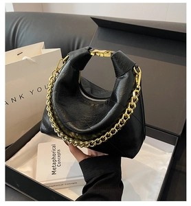 Detail of black quilted shoulder bag featuring gold chain strap and metallic buckle closure