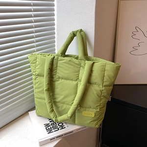 Light green quilted down tote bag with a contrast yellow fashion tag on a window sill