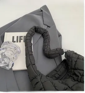 Close-up of black quilted cloud bag texture and handle on a grey suit background