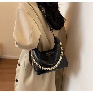 Detail of black quilted hobo bag featuring gold chain and leather strap on trench coat