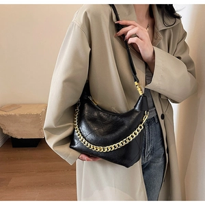 Détail d'un sac hobo en cuir noir grainé avec chaîne dorée porté sur un manteau beige