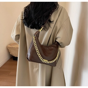 Sac à bandoulière matelassé marron foncé avec chaîne dorée porté sur un trench-coat