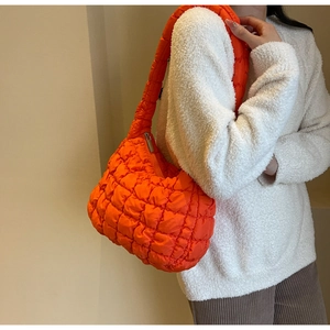 Close-up of orange quilted puffer crossbody bag with soft textured rhombs and wide strap