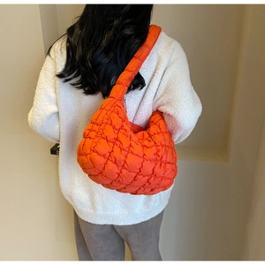 Detail of bright orange quilted puffer bag texture with wide shoulder strap and zipper