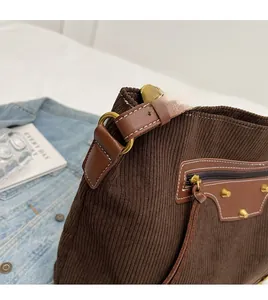 Detail of brown corduroy tote bag featuring white stitching and gold metal rivet accents