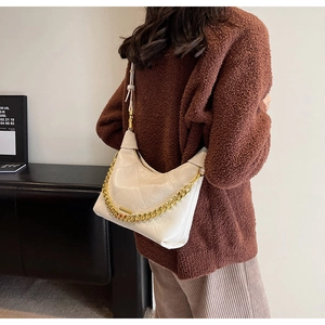 Détail d'un sac bandoulière beige matelassé avec chaîne dorée porté par un mannequin