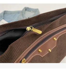 Detail of dark brown corduroy tote with golden zipper and metal rivet hardware