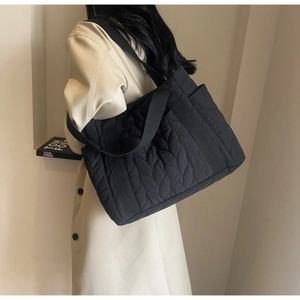 Detailed side view of black quilted puffer tote bag with leaf pattern stitching and strap