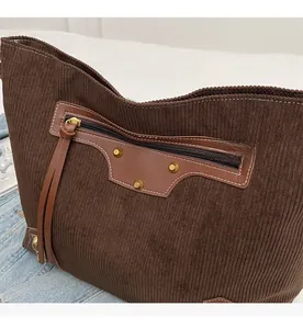 Detail of brown corduroy tote featuring a leather zip pocket with metal rivets