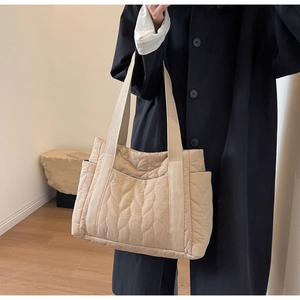 Close-up of beige quilted tote bag showing wave stitching and side pocket detail