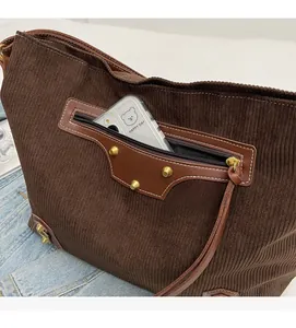 Close-up of brown corduroy tote bag featuring front zip pocket and gold rivet detail