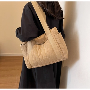 Close-up of beige quilted tote bag showing intricate leaf-pattern stitching and wide strap