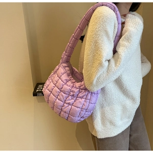 Quilted puffy shoulder bag in purple nylon fabric worn by a model in casual home setting
