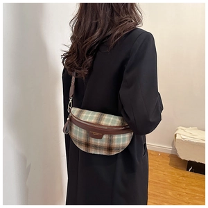 Détail du sac banane croissant à carreaux vert et marron porté sur un blazer noir
