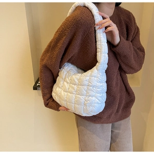 Detail of white quilted puffy shoulder bag with soft nylon texture worn by a model