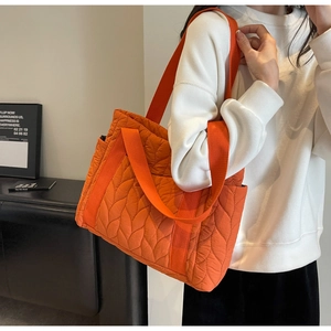 Detail of orange quilted tote bag featuring padded leaf patterns and wide nylon strap