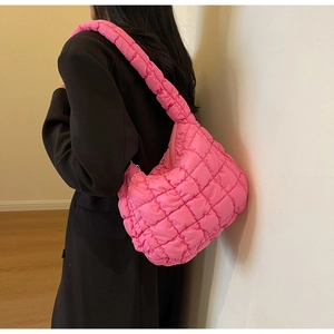 Bright pink quilted cloud bag with puffy shoulder strap shown on model in a side view
