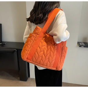 Close-up of orange quilted tote bag with leaf texture and wide fabric shoulder strap